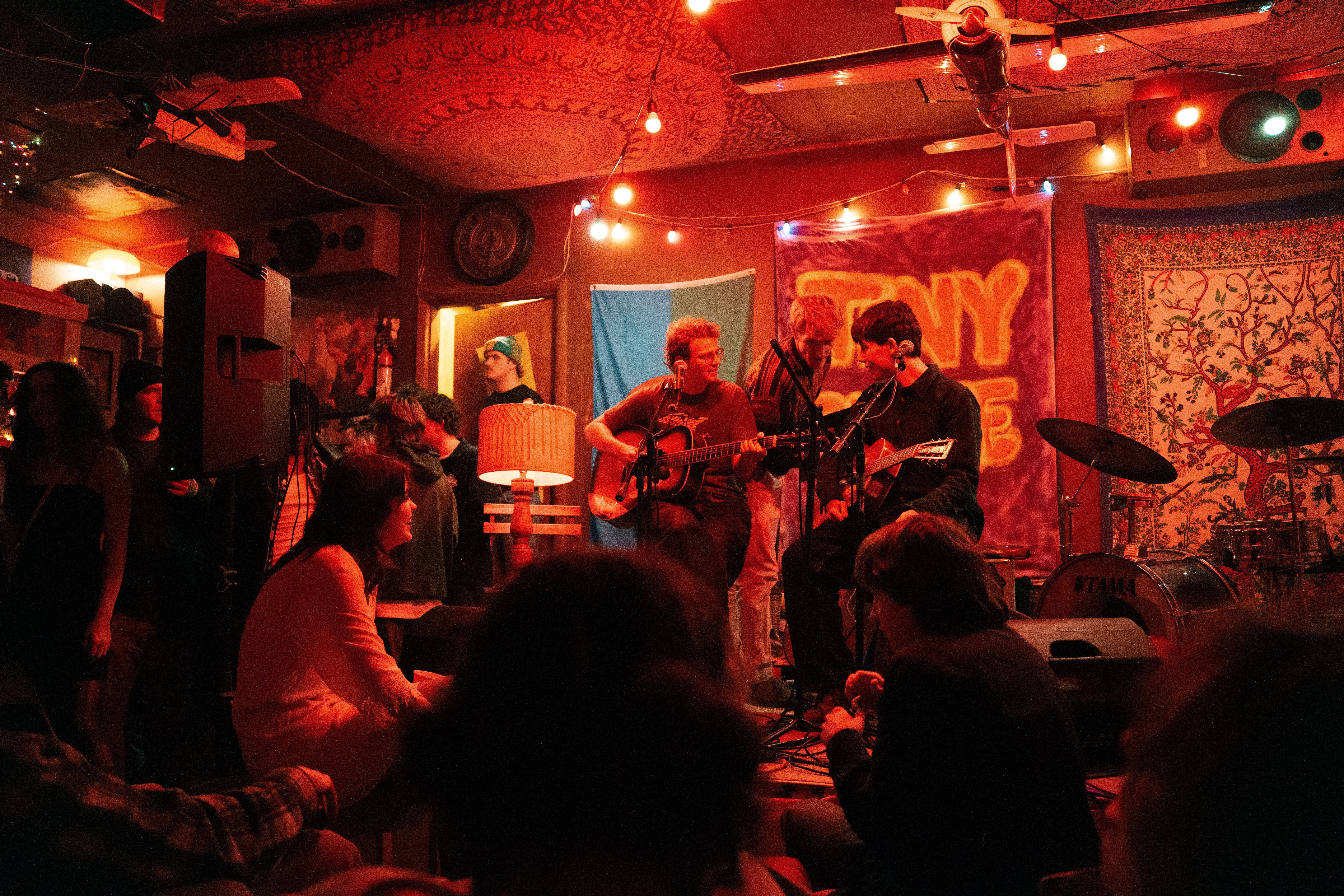 Band playing in a warmly lit garage, with a crowd surrounding the stage.
