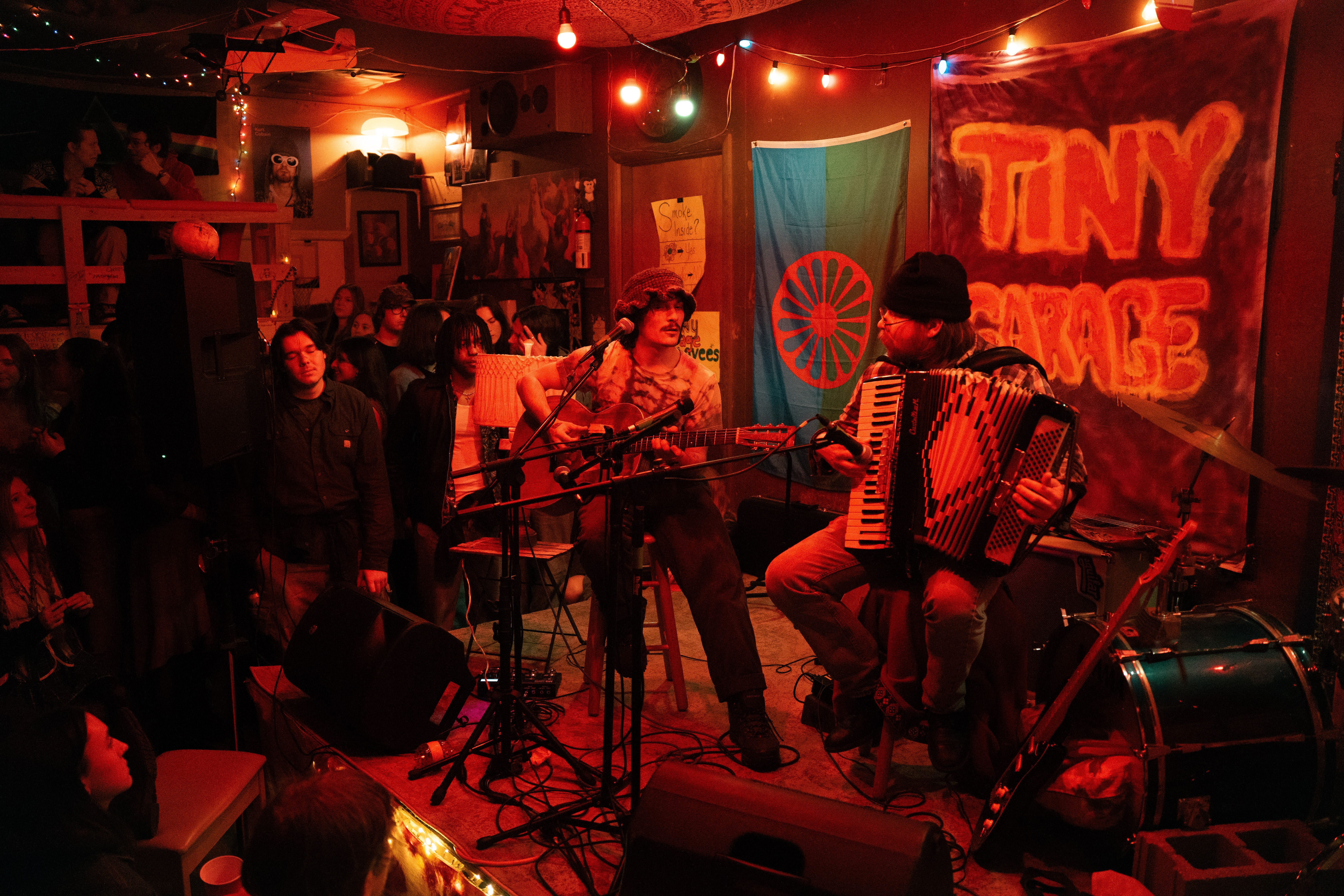 Band playing in a warmly lit garage, with a crowd surrounding the stage.