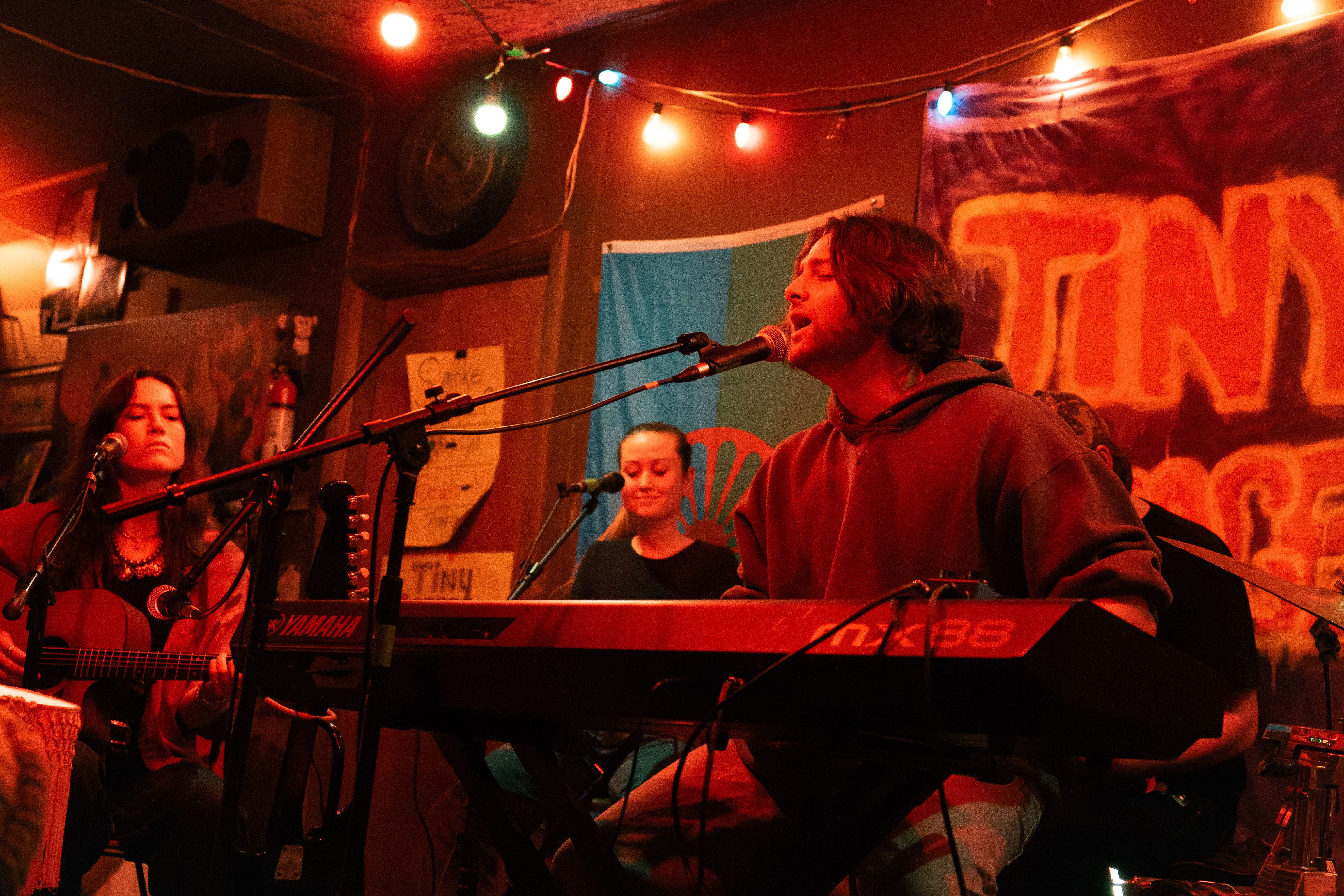 Band playing in a warmly lit garage, with a crowd surrounding the stage.