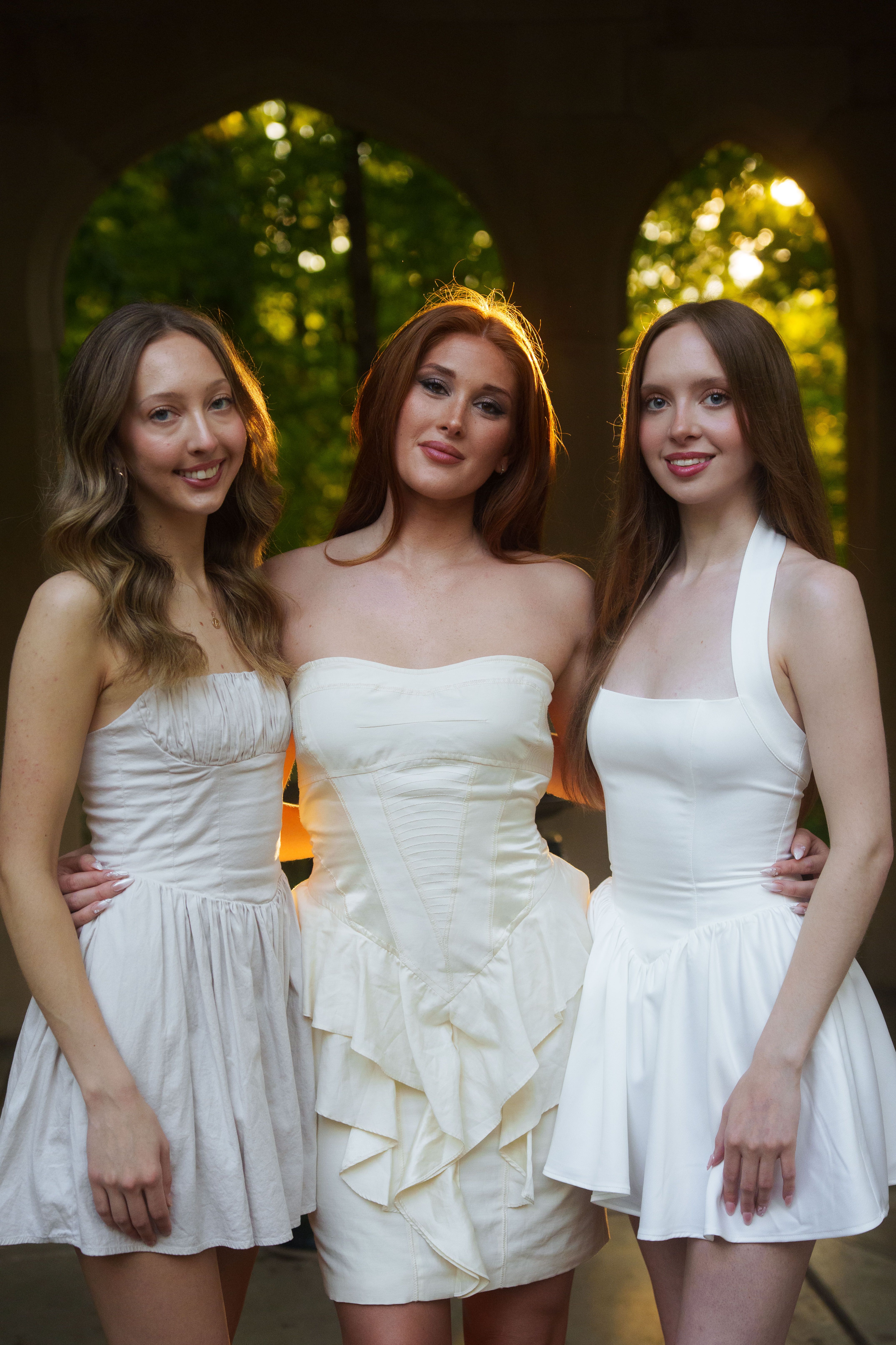 Three graduates in white dresses at sunset.
