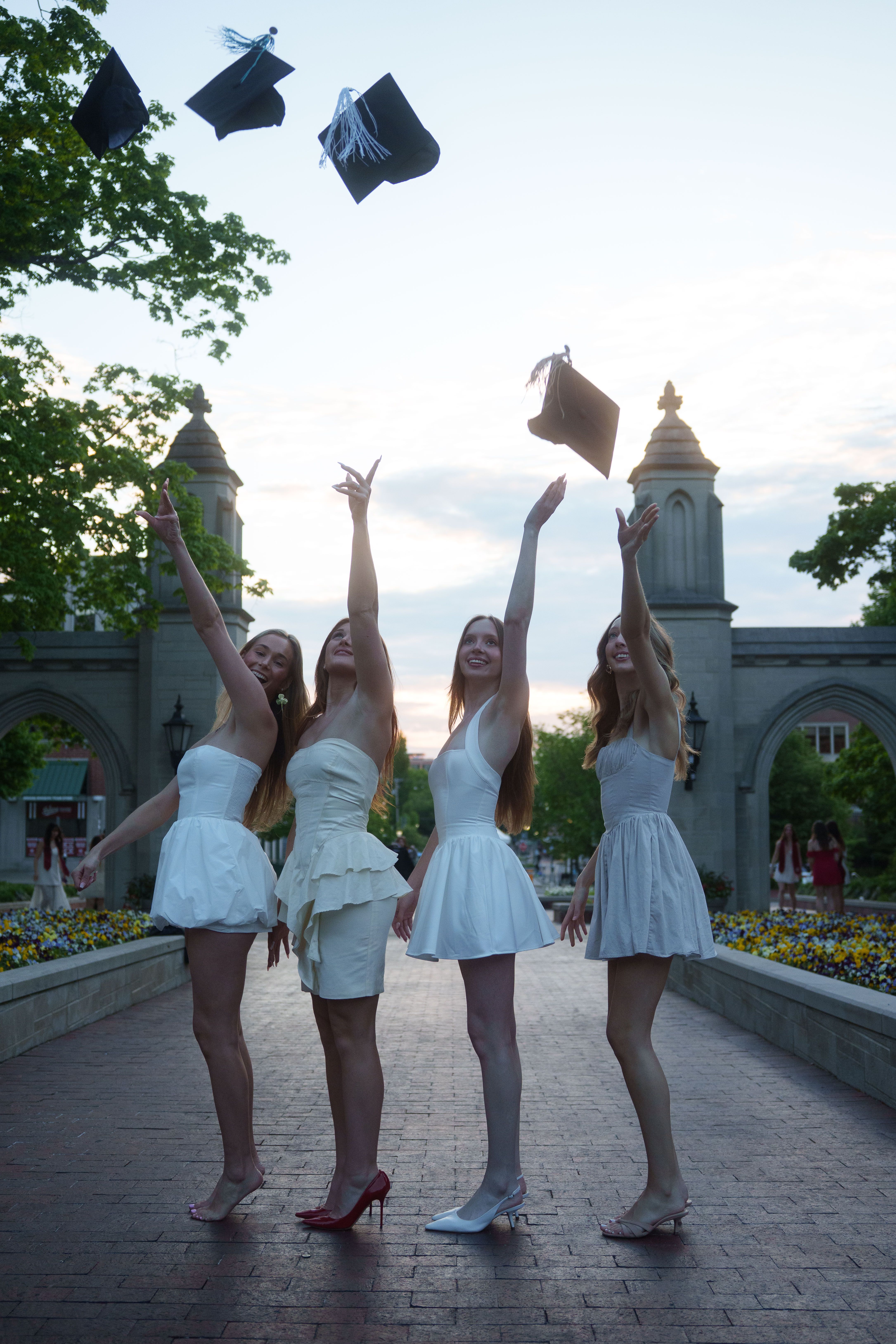 Three graduates in white dresses at sunset.