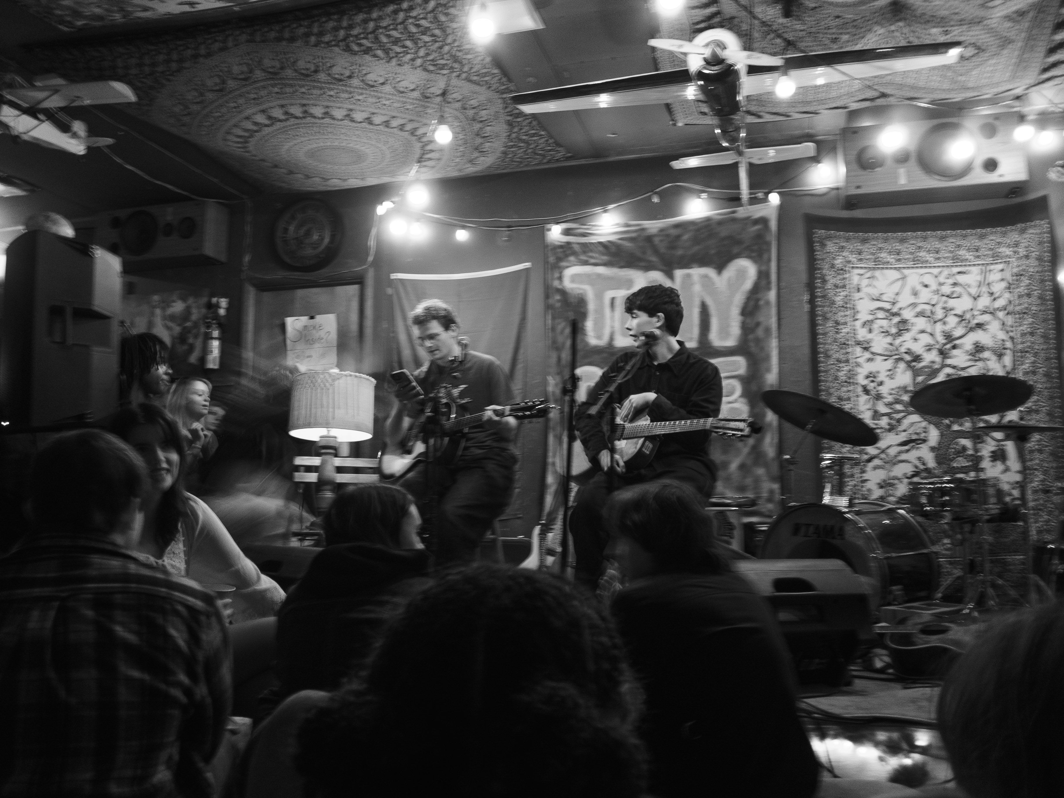 Band playing in a warmly lit garage, with a crowd surrounding the stage.